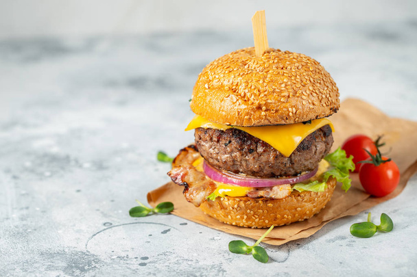 A set of homemade delicious burgers of beef, bacon, cheese, lettuce and tomatoes on a light concrete background. Fat unhealthy food close-up. With copy space - Photo, image