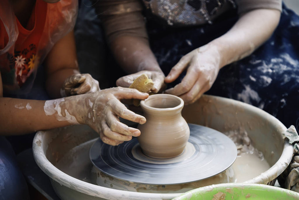 Nahaufnahme von Frauen und jungen Mädchen, die an der Töpferscheibe arbeiten. Hände formen einen Tontopf, selektiver Fokus. Lehm-Modellierungsstunde   - Foto, Bild