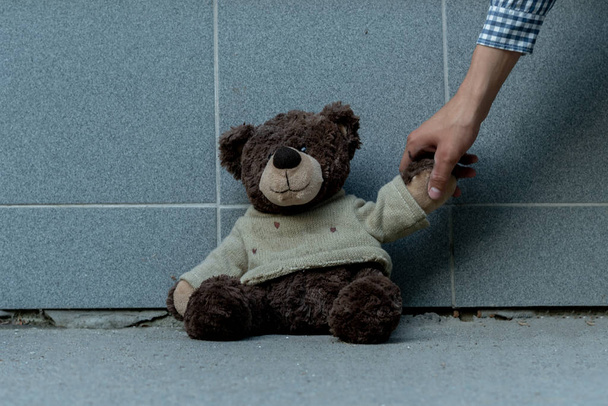 mão humana agarrar o urso de pelúcia sujo do chão ao ar livre, conceitos perdidos - Foto, Imagem