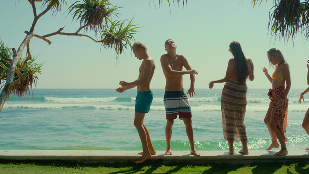 Twee atletische jongens en drie prachtige meiden dragen zwem shorts en bikini dans terwijl ze op de pier staan met een diep vervaagd uitzicht op de zeehaven. Groep jonge mensen dansen en plezier hebben op vakantie - Video