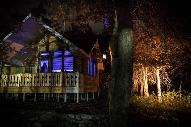 Old house with a Ghost in the forest at night or Abandoned Haunted Horror House in fog. Old mystic building in dead tree forest. Trees at night with moon. Surreal lights. Horror Halloween concept - Photo, Image
