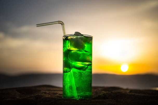 Close-up nat glas van groene koude Mint drankje, kleurrijke oranje zonsondergang achtergrond op het terras. Koeling zomer drankje. Zomer fris en koel inspiratie, avond contrast kleurencombinatie. - Foto, afbeelding