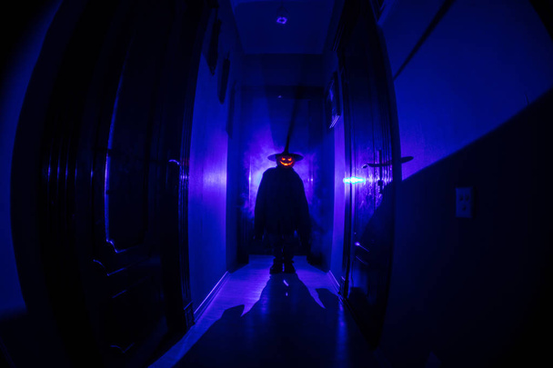 Halloween-Konzept. Gruselige Silhouette im dunklen Gang mit Kürbiskopf. getöntes Licht mit Nebel auf dem Hintergrund. Selektiver Fokus - Foto, Bild