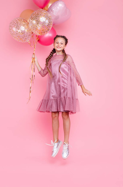 Happy teenage girl jumping high with balloons isolated on pink b - Zdjęcie, obraz