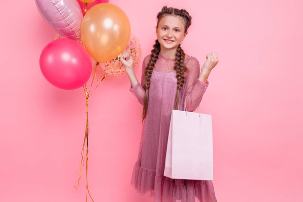 Happy girl with balloons and shopping bags posing on a pink back - Фото, зображення