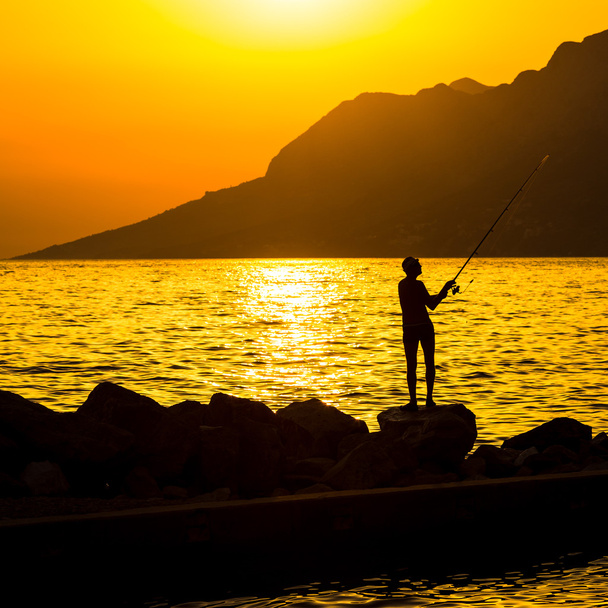 Fisherman's silhouette on the beach at colorful sunset - 写真・画像