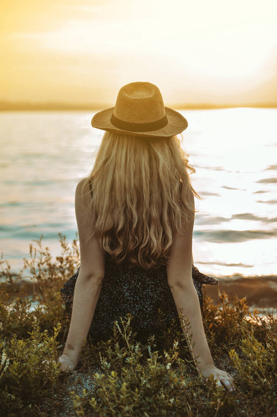 Mulher elegante em chapéu caminha na praia ao pôr do sol
. - Foto, Imagem