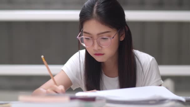 Asyalı öğrenci kadınlar üniversitede kütüphanede kitap okuyor. Üniversite kampüs konseptinde ders masasında bilgi için çok çalışırken genç lisans kız stres yorgun sorun var. Yavaş çekim. - Video, Çekim