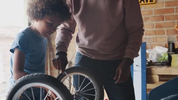Middle aged black father and his pre teen son standing at a workbench building a racing kart together in their garage, close up, mid section of father - Metraje, vídeo