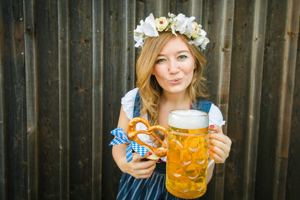 beautiful smiling young woman in traditional bavarian clothing holding beer mug and pretzel - Photo, image