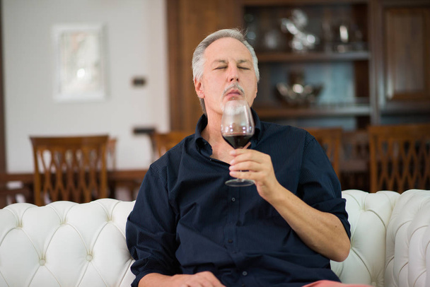 Portrait of a mature man enjoying a glass of red wine at home - Foto, afbeelding