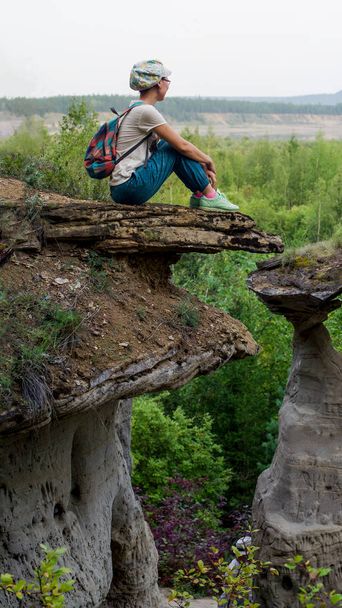 Yakut chica asiática con gafas sentadas en el borde de un acantilado junto a las atracciones - forma de relieve erosión de hongos en el fondo de abeto etiqueta salvaje del norte de Rusia
. - Foto, Imagen