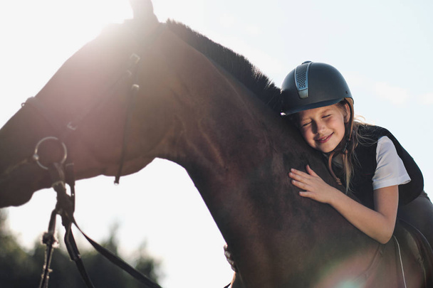 Girl teenager jockey sits on a brown horse, hugs and strokes her. - Φωτογραφία, εικόνα
