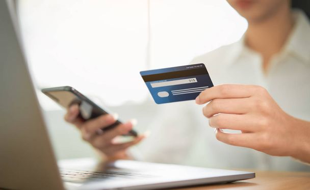 Woman shopping online on smartphone and holding back view of the credit card and enter the payment code for the product. - Photo, Image