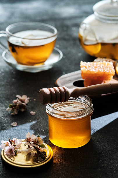 Een potje honing met honingraten en een stok, een theepot met een kopje  - Foto, afbeelding