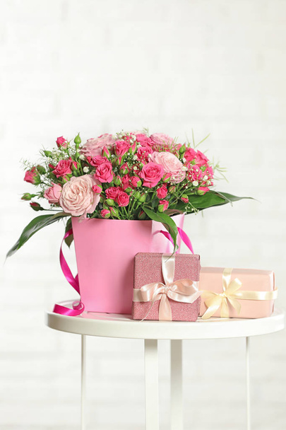 Beautiful bouquet of flowers and gift boxes on table against light background - Photo, Image