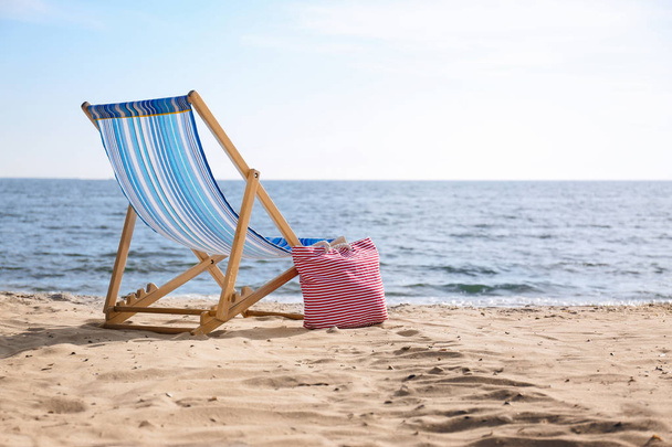 Lounger and bag on sand near sea, space for text. Beach objects - Фото, зображення