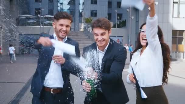 Csoport izgatott üzletemberek ünneplők egy üveg pezsgőt és pirítás a siker kültéri modern Business Office Center háttérben. - Felvétel, videó
