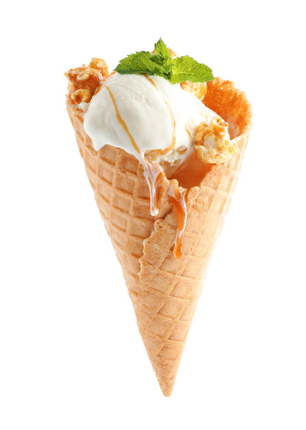 Delicious ice cream with caramel sauce, mint and popcorn in waffle cone on white background - Photo, Image