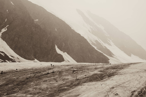 At mountains foothills on the glacier are alpenists. Toned photo of the beautiful nature of the snowy mountains of Altai. Little people. Aktru Glacier. Mountain Altai.  Russia. Toned sepia photo - Photo, image