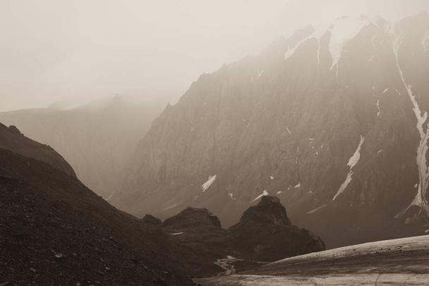 A large number of stones on top. Mountain peaks in the misty clouds. Beautiful views of high snow-capped mountains and a glacier on a tourist trip through the nature of Altai land. Toned sepia photo. - Foto, afbeelding