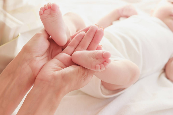 Anne elinde bebeğinin ayaklarını tutar, kapalı, bulanık arka plan - Fotoğraf, Görsel
