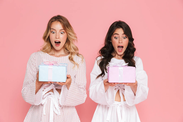 Happy young two pretty women girls friends sisters posing isolated over pink wall background holding present boxes. - Foto, Imagem