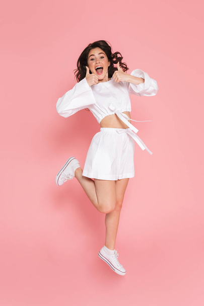 Happy young excited emotional woman jumping isolated over pink wall background. - Фото, изображение