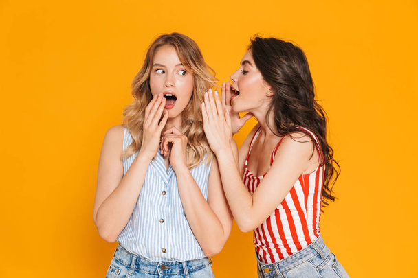 Portrait of two caucasian blonde and brunette women 20s in summer wear expressing surprise while whispering gossips - Fotografie, Obrázek