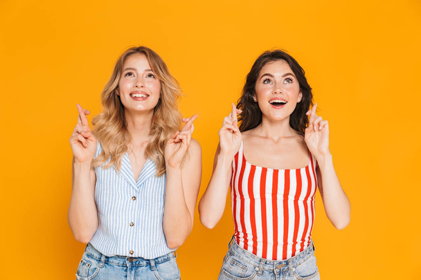 Portrait of two happy blonde and brunette women 20s in summer wear dreaming while keeping fingers crossed - Φωτογραφία, εικόνα