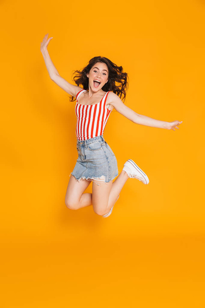Portrait of delighted brunette woman in denim skirt jumping with throwing up arms - Fotografie, Obrázek