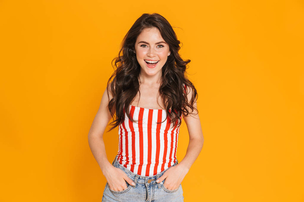 Portrait of cute brunette woman 20s in striped t-shirt smiling at camera with her hands in her pockets - Fotoğraf, Görsel