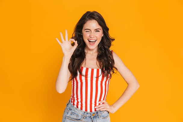 Portrait of cheerful brunette woman in striped t-shirt winking at camera and showing ok sing - Fotoğraf, Görsel