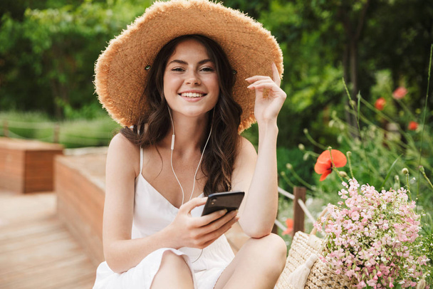 Photo of beautiful young woman wearing straw hat listening to mu - Zdjęcie, obraz