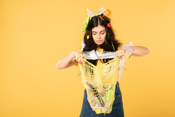 chica emocional con la basura en la bolsa de sujeción de pelo con basura aislado en amarillo
 - Foto, Imagen