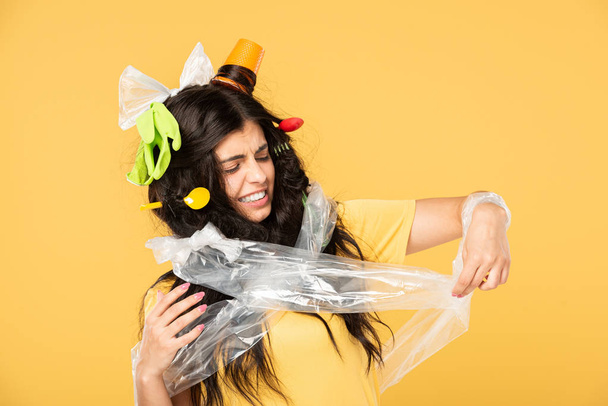 ανήσυχη νεαρή γυναίκα με σκουπίδια στα μαλλιά απομονώνονται σε κίτρινο - Φωτογραφία, εικόνα