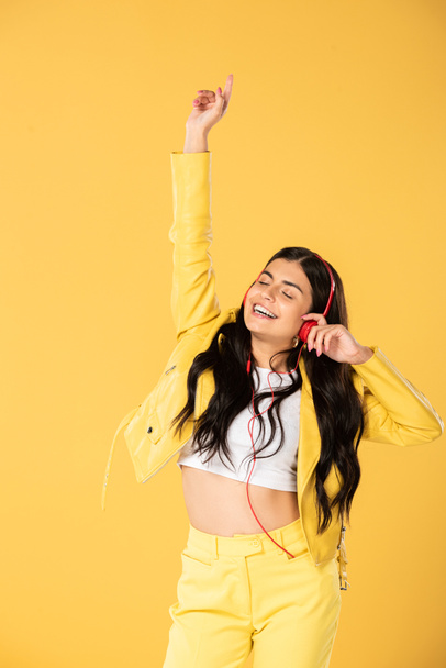 happy girl dancing and listening music with headphones, isolated on yellow  - Photo, Image