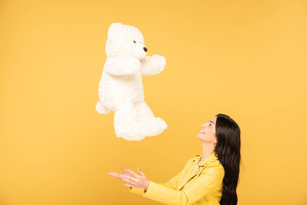 pretty young woman throwing up teddy bear, Isolated On yellow - Photo, Image