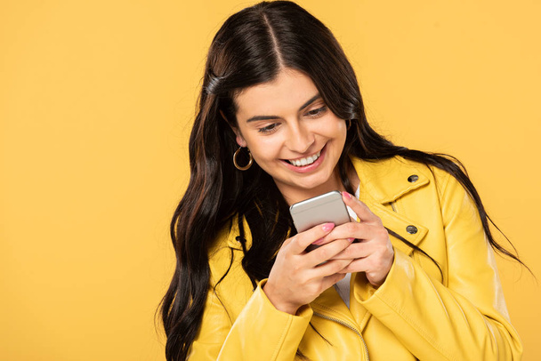 attractive brunette girl using smartphone, isolated on yellow - Фото, зображення