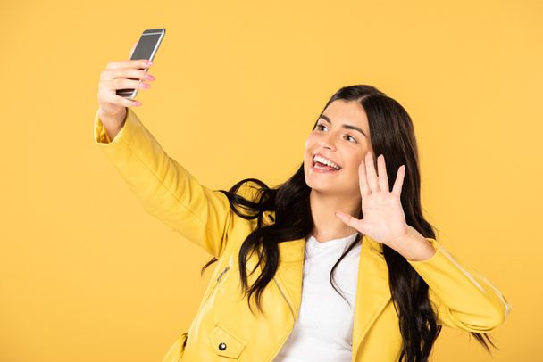 brunette girl waving and having video chat on smartphone, isolated on yellow - Foto, Bild