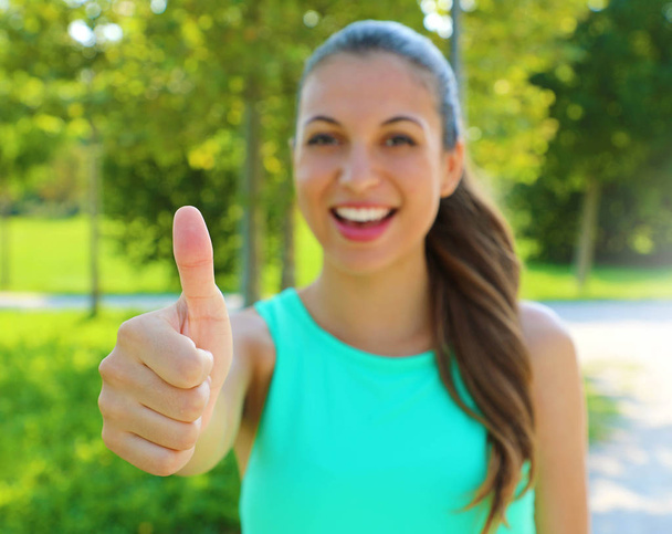 It's ok! I like it! Portrait of winner girl showing thumb up. Positive smiling fitness healthy woman outdoor. Focus on the hand. - Photo, Image