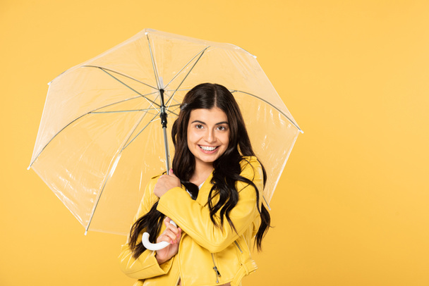 krásná usměvavá dívka s průhledným deštníkem, izolovaná na žluté - Fotografie, Obrázek