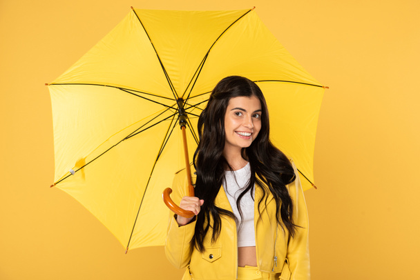 beautiful smiling girl posing with umbrella, isolated on yellow - Фото, изображение