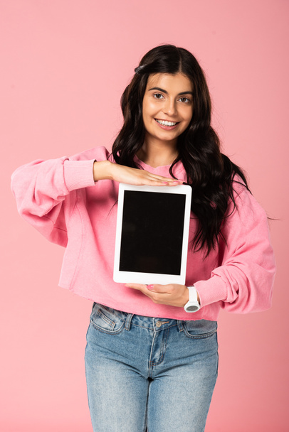 glimlachend meisje presenteert digitale tablet met blanco scherm, geïsoleerd op roze - Foto, afbeelding