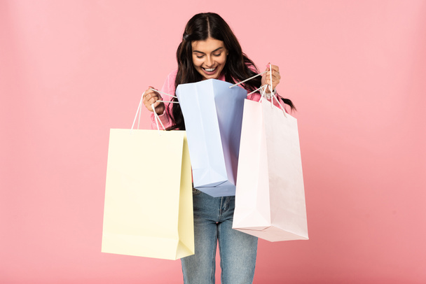 aantrekkelijk glimlachend meisje houdt boodschappentassen, geïsoleerd op roze - Foto, afbeelding