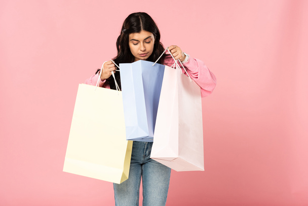όμορφο κορίτσι ψάχνει σε σακούλες για ψώνια, απομονωμένη σε ροζ - Φωτογραφία, εικόνα