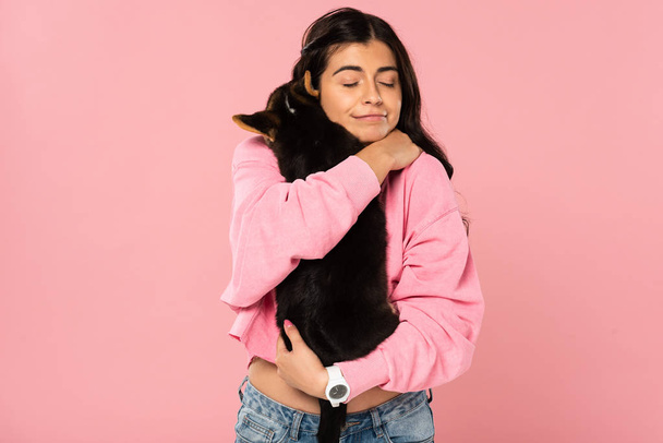 fröhliches Mädchen umarmt niedlichen Welpen, isoliert auf rosa - Foto, Bild