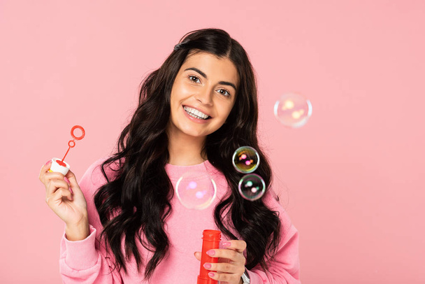 cheerful girl with soap bubbles isolated on pink - 写真・画像