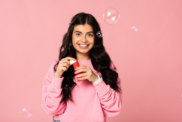 attractive happy young woman playing with soap bubbles isolated on pink - Foto, Bild