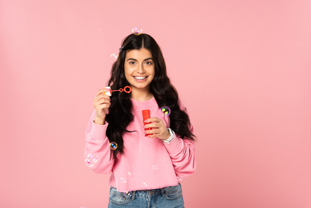 smiling girl playing with soap bubbles isolated on pink - Foto, afbeelding